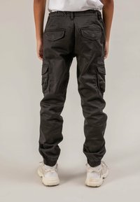 Pantalon cargo noir avec poignets élastiques aux chevilles, plusieurs poches et une coupe décontractée. Le tissu présente une légère brillance avec une finition texturée.