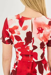Rotes Kleid mit floralem Muster, kurze Ärmel, weicher Stoff. Schlüsselrückseite mit einem kleinen Knopf. Enthält verschiedene Rottöne und Weiß.