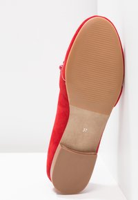 Chaussure plate rouge inclinée verticalement, montrant une semelle lisse couleur camel avec des lignes discrètes antidérapantes et la taille 37 imprimée près du petit talon.