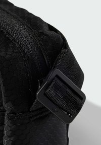 Czarny materiał z wzorem w sześciokąty o fakturowanym wykończeniu, z zamkiem błyskawicznym oraz czarną klamrą po boku.