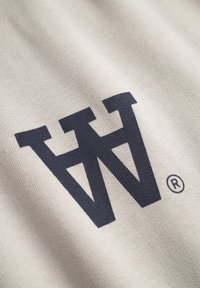 Beige fabric features a prominent dark navy logo resembling stylized letters "W" and "W", with a small registered trademark symbol.