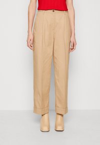 Pantalons beige à jambe large en tissu léger, dotés d'une taille haute, de plis et de poignets roulés, associés à des talons compensés crème.