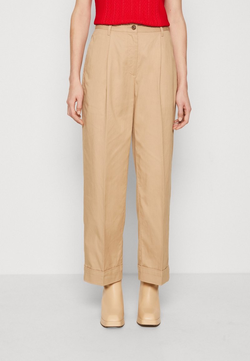 Pantalons beige à jambe large en tissu léger, dotés d'une taille haute, de plis et de poignets roulés, associés à des talons compensés crème.