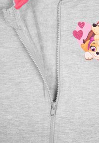 Felpa grigia con zip caratterizzata da una cerniera lucida, tessuto morbido e una grafica di un cane cartone con un accento di cuore rosa nella parte anteriore.