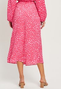 Růžová midi sukně vyrobená z lehké látky, pokrytá rozptýleným bílým tečkovaným vzorem, mírně se rozšiřující od pasu s volným lemem.