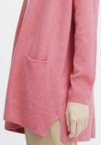 Cardigan a maniche lunghe, aperto davanti, in morbido maglione rosa chiaro. Caratterizzato da una sola tasca applicata, polsini a coste e spacco laterale nell'orlo.