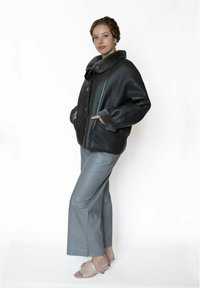 Zwarte leren jas met een grijze nepbontkraag, voorzien van grote knopen en zijzakken. Gecombineerd met grijze leren broek en lichte sandalen.