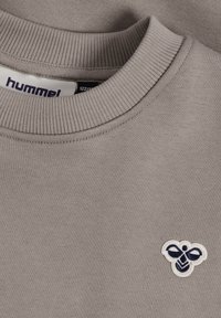 Lysegrå crewneck-sweatshirt med en lille marineblå og hvid bi-logo broderet på brystet og et "hummel" mærke inde i kraven.