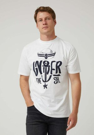 Camisa de algodón blanca con un audaz diseño gráfico en azul marino que presenta un ancla, un barco y el texto "Bajo el Mar". Cuello redondo y mangas cortas.