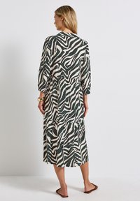Vestito verde e avorio con motivo, gonna a strati, maniche lunghe e vestibilità rilassata. Il tessuto appare leggero e fluido.