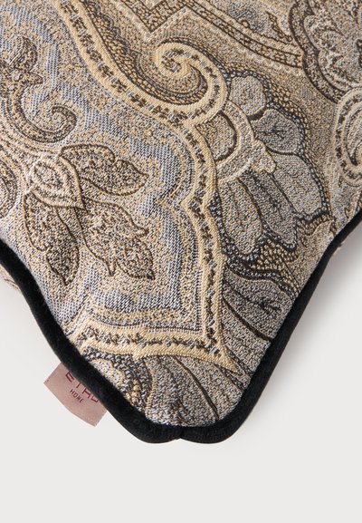 Coin de coussin décoratif avec un motif tapisserie floral et paisley complexe en beige, or et gris, bordé d’un liseré noir.