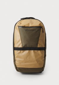 Backpack in tan and olive green with grid pattern, featuring a black zippered pocket, adjustable straps, and durable fabric.