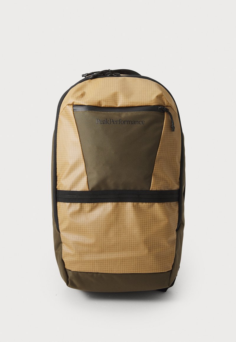 Backpack in tan and olive green with grid pattern, featuring a black zippered pocket, adjustable straps, and durable fabric.