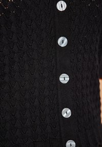 Maglione nero a maglia con un motivo a diamante testurizzato e sei bottoni rotondi di colore chiaro lungo la patta anteriore.