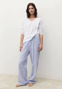 Camicia bianca a maniche lunghe con scollo a V abbinata a pantaloni larghi blu e bianchi a righe, dotati di una cintura elastica e di un tessuto morbido.