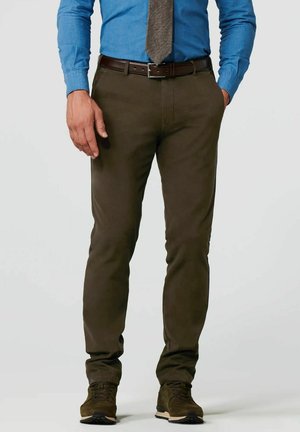 Man die een bruine broek, bruine riem, blauw overhemd, grijze stropdas en bruine sneakers draagt, staand met één hand in de broekzak tegen een effen achtergrond.