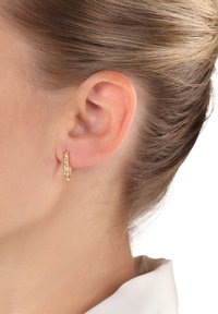 Pendiente de aro dorado con un patrón texturizado, exhibido en la oreja de un modelo, mostrando su diseño circular y acabado pulido.
