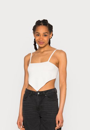 Top cropped branco, texturizado, com alças finas e uma bainha assimétrica, combinado com jeans pretos de cintura alta. Design simples e moderno.
