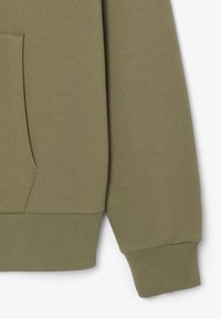 Felpa verde oliva con tasca a marsupio, polsini a coste e materiale in cotone morbido. La texture è liscia con un design minimalista.