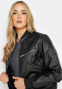 Svart läderbomberjacka med ribbade muddar, framsidans dragkedja och en liten bröstficka med dragkedja. Slät textur, skräddarsydd passform.