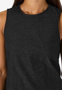 Melnā bezpieņu kreklā ar apaļu dekoltē. Izgatavots no teksturētas šķiedras, ar smalkām šuvēm un gludu apdari.