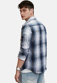 Blå- og hvidmønstret skjorte med plaid-design, lange ærmer og knap-ned krave. Båret med lyse denimjeans og et ur.