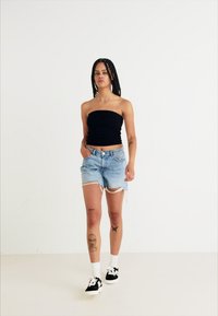 Czarny top bez ramiączek, jasnoniebieskie podarte szorty dżinsowe, białe skarpetki do kostek i czarne adidasy. Minimalistyczny design z widocznymi tatuażami na nogach.