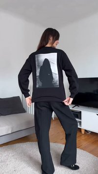 Μαύρο φούτερ με μια μεγάλη γκρι φωτογραφία στην πλάτη, που απεικονίζει μια φιγούρα με μακριά μαλλιά σε σιλουέτα πάνω σε ένα υφασμένο φόντο.