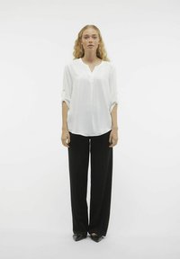 Hvid, langærmet skjorte med knapper og V-hals, med optrukne manchetter, parret med sorte, brede bukser. Glat tekstur, minimalisk design.