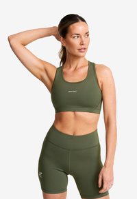 Olivgrön sportbhn och matchande shorts i elastiskt material. Bh:n har en rund halsringning och logodetaljer. Slät yta.