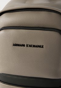 Μπροστινή όψη σακιδίου πλάτης από ταμπά υφή δέρμα με μαύρο φερμουάρ και λογότυπο Armani Exchange σε μαύρα γράμματα.
