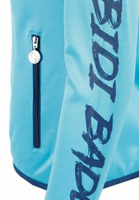 Lichtblauwe jas mouw met een donkerblauwe ritssluiting en "RADICAL" verticaal gedrukt in vet, versleten donkerblauwe letters.