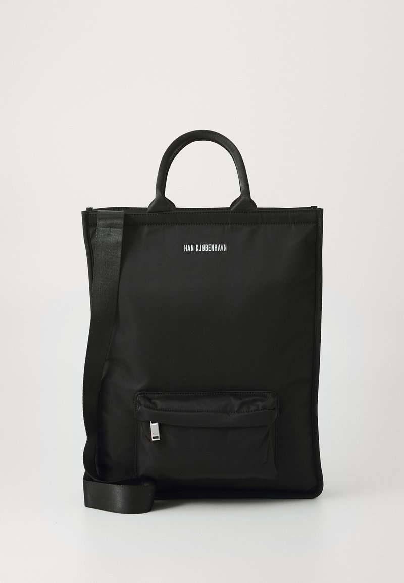 Black nylon tote bag with flat shape, two short handles, detachable strap, front zip pocket, and printed brand name. Smooth texture.