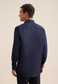 Camicia button-up blu navy con maniche lunghe, texture liscia, colletto classico e leggera lucentezza, con orlo arrotondato e polsini abbottonati.