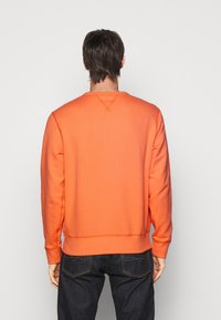 Orange sweatshirt med långa ärmar, rund halsringning och ribbade muddärmar. Mjuk textur och synliga sömdetaljer. Bärs med mörka jeans.
