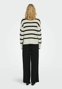 Strickpullover in Creme mit schwarzen horizontalen Streifen, abgerundetem Saum, kombiniert mit schwarz weit geschnittenen Hosen, von hinten betrachtet.