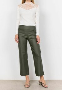 Biały top z długim rękawem z koronkową wstawką, zestawiony z oliwkowozielonymi spodniami o szerokich nogawkach. Materiał o fakturze, dopasowana talia oraz wzorzyste sandały.