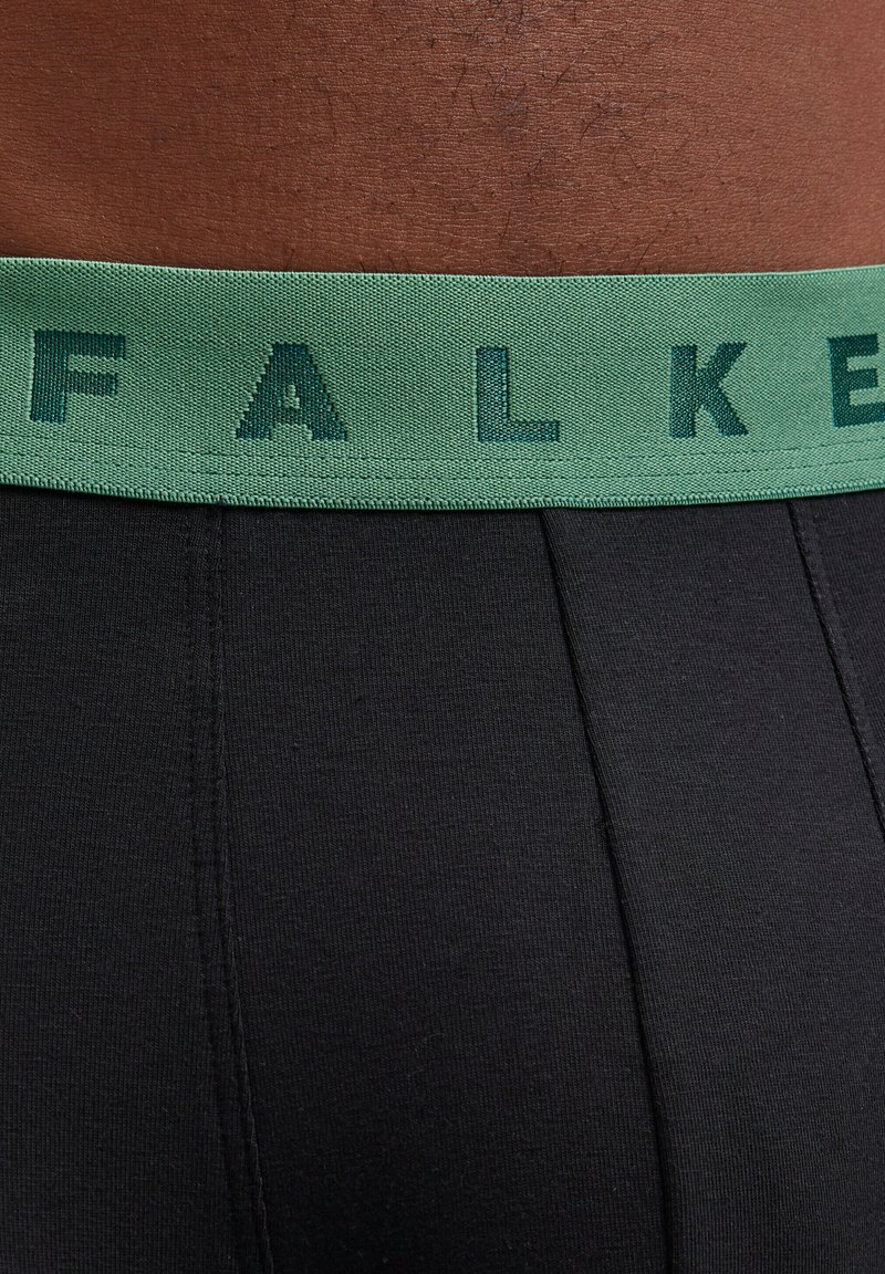 Zwarte boxershorts met een geprofileerde groene elastische tailleband waarop de merknaam "FALKE" in donkergroene letters staat.