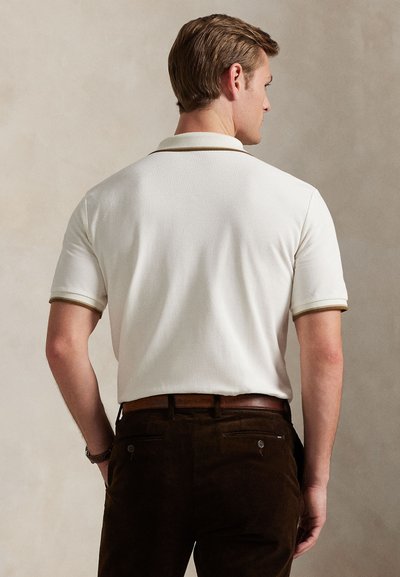 Krátký rukáv polokošile v krémové barvě s texturovaným povrchem, s kontrastním hnědým límcem a manžetami, doplněná tmavě hnědými manšestrovými kalhotami.