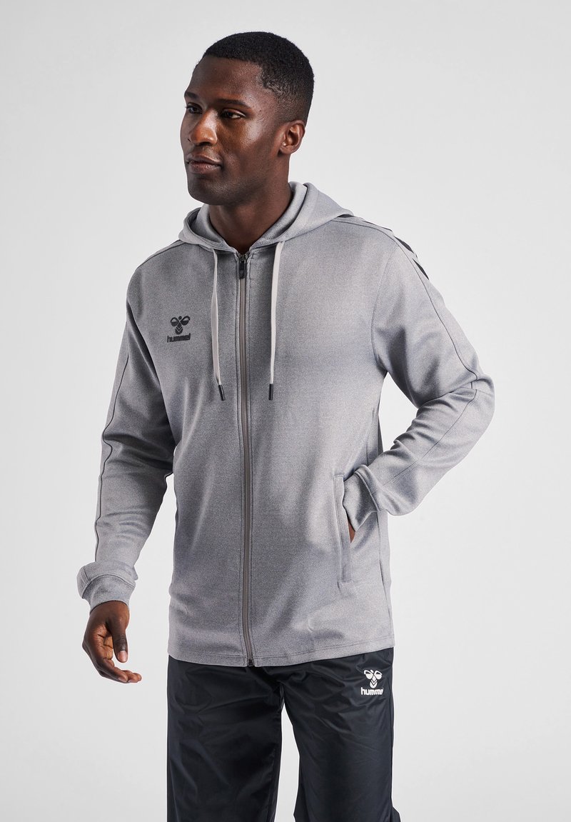 Sudadera gris con cremallera, fabricada con un tejido texturizado, capucha ajustable con cordón y bolsillos laterales, que presenta un pequeño logo en el lado izquierdo del pecho.