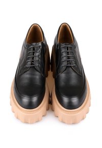 Chaussures en cuir noir à lacets avec des semelles en caoutchouc beiges épaisses, présentant une texture lisse et un design à bout rond. Couture détaillée sur la tige.