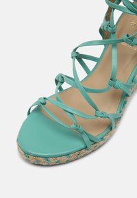 Sandale espadrille en daim bleu canard avec des brides entrecroisées, un bout arrondi et une semelle en jute tressé ornée d'accents turquoise et dorés.