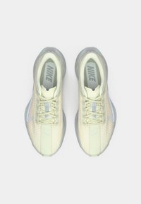 Αθλητικά παπούτσια Nike με ελαφρώς κιτρινωτό δίχτυ ως επάνω μέρος, γκρι κορδόνια και διαφανές γκρι πέλμα. Διαθέτουν έντονο λογότυπο και διάτρητη υφή.