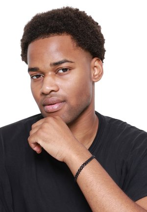 Bracelet tressé noir porté au poignet, avec un design texturé. La personne a les cheveux courts et bouclés et porte une chemise noire.