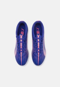Fioletowe buty sportowe z różowymi akcentami, smukły design, teksturowana syntetyczna cholewka oraz wyraźny wzór pasków. Posiadają system sznurowania.