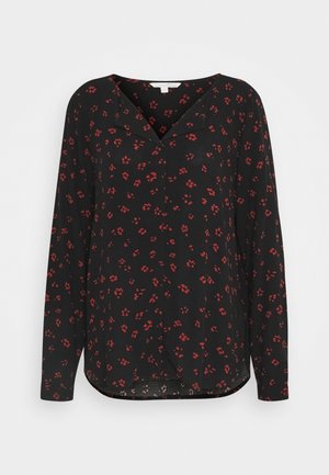 Blouse noire à manches longues avec petit motif floral rouge et col en V, présentée sur un fond blanc uni.