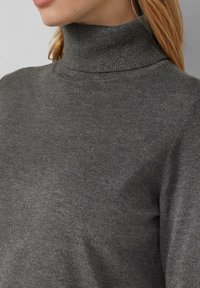 Pull en maille gris avec un col montant près du cou, texture douce et léger éclat, arborant un design simple sans embellissements supplémentaires.