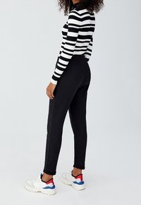 Sorte joggers med tapered fit, parret med en langærmet top i sort og hvid stribe. Hvide sneakers med røde og blå detaljer fuldender looket.