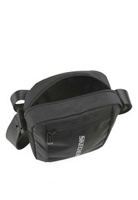 Bolso bandolera negro con cierre superior, material de tela, forma rectangular y logo de Skechers en la parte frontal. Incluye correa ajustable.