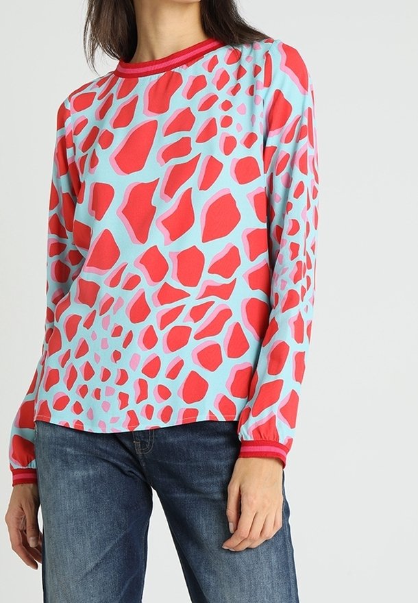 Pitkähihainen vaate vaaleansinisellä pohjalla, jossa on punainen ja vaaleanpunainen abstrakti kuvio. Varustettu ribatulla punaisella kaula-aukolla ja elastisilla hihansuilla.